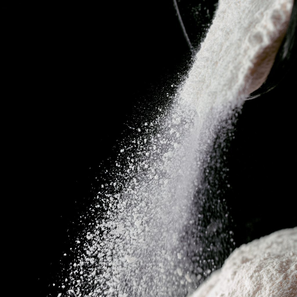 White powder being poured from a container against a black background, creating a cascading stream of fine particles